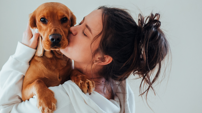 home-staging_01 Auf dem Bild sieht man eine braunhaarige Frau in weißer Bluse, die einen Welpen am Arm hat und ihn verliebt küsst